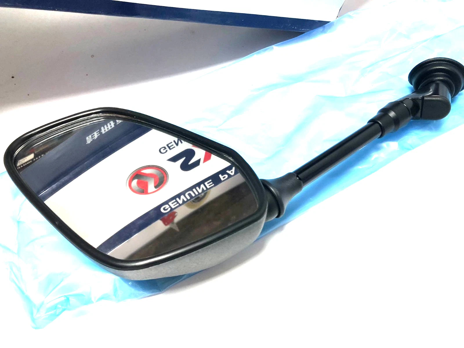 Black rectangular mirror with “nos Sym CITYCOM 300 RH” text, blue casing, and attached black side handle.