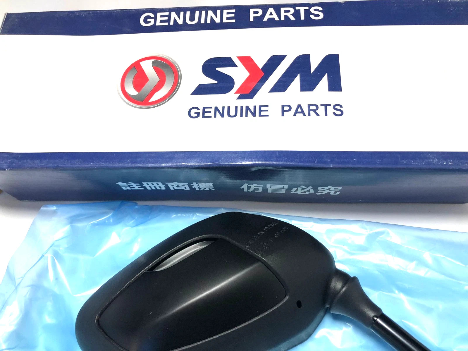 Black plastic Sym CITYCOM 300 RH mirror part on blue box labeled “Genuine Parts” with white text in Chinese.